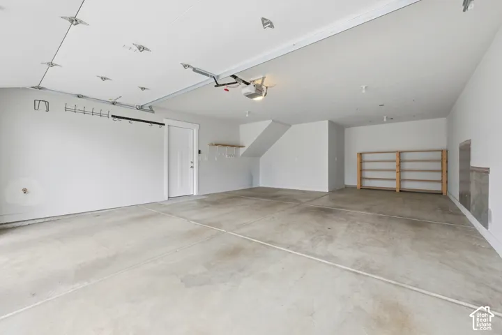 Spacious garage featuring a concrete floor, white painted walls, exposed ceiling tracks, and built-in wooden shelving units