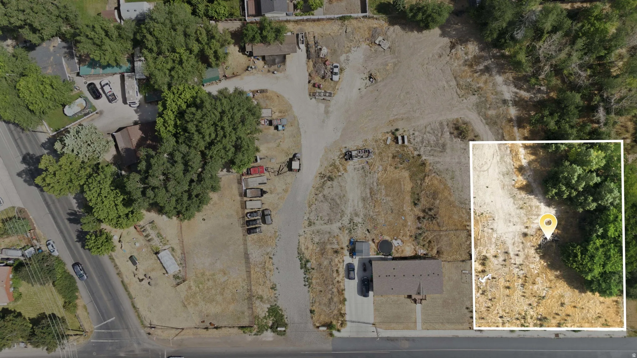 Aerial perspective showcasing extensive land with a single-story residence featuring a dark-toned roof