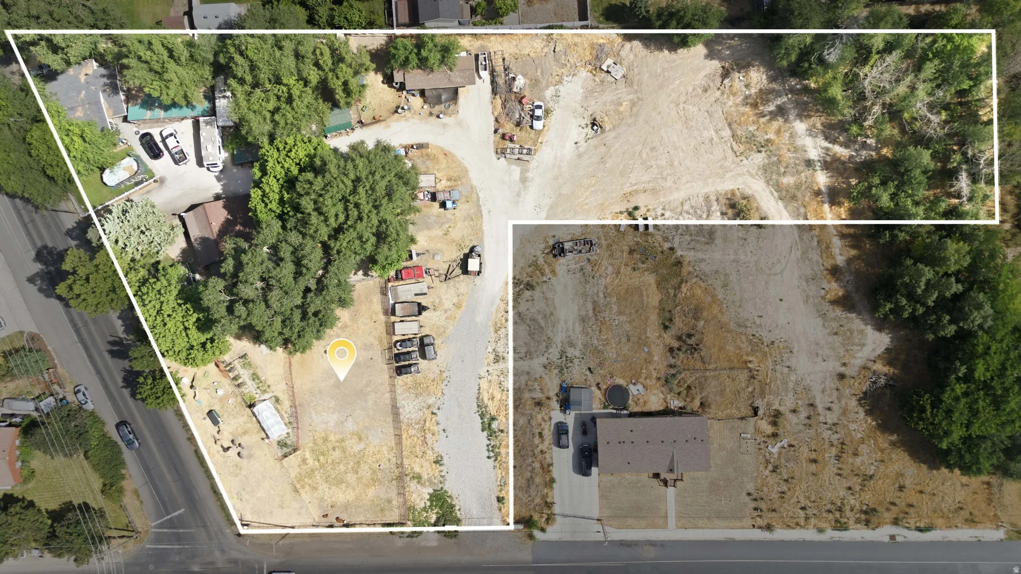 Expansive land parcel featuring a central gravel driveway, mature trees providing natural shading, and a combination of cleared and partially treed areas