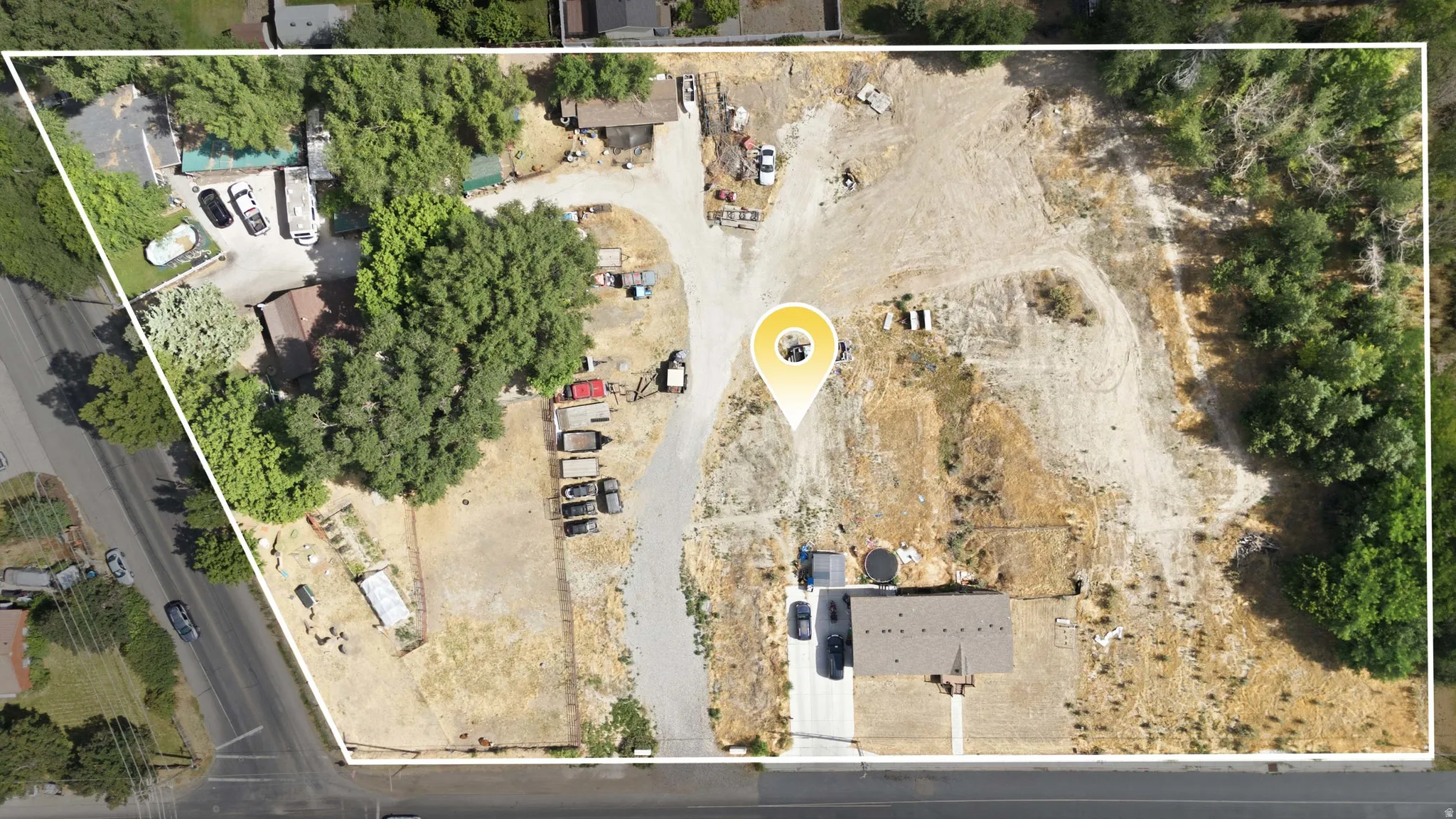 Expansive aerial showcasing a significant land parcel featuring a single-story residence with a brown shingle roof, established trees, and a substantial undeveloped area