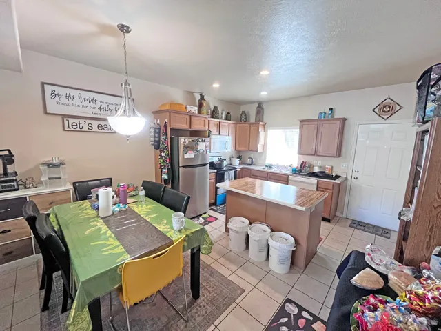 Open-concept kitchen and dining area featuring recessed lighting, a central kitchen island with a wood-finish countertop, light wood cabinetry, and a stainless steel refrigerator