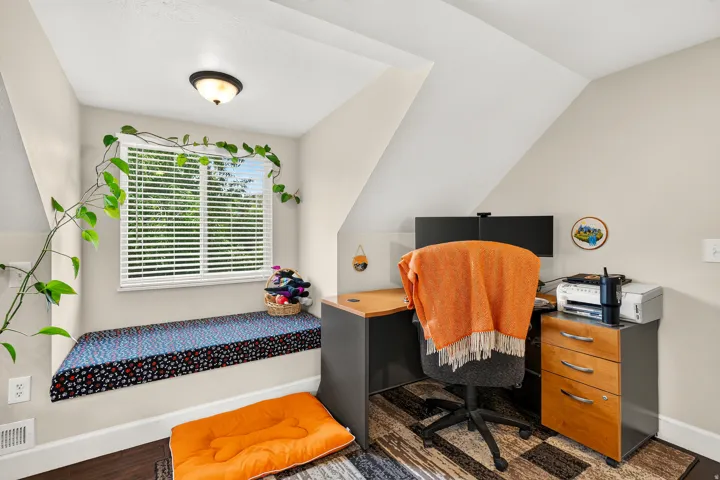 Integrated window bench with cushion, recessed window with blinds, sloped ceiling, wood-finish flooring, and a flush-mount ceiling light fixture