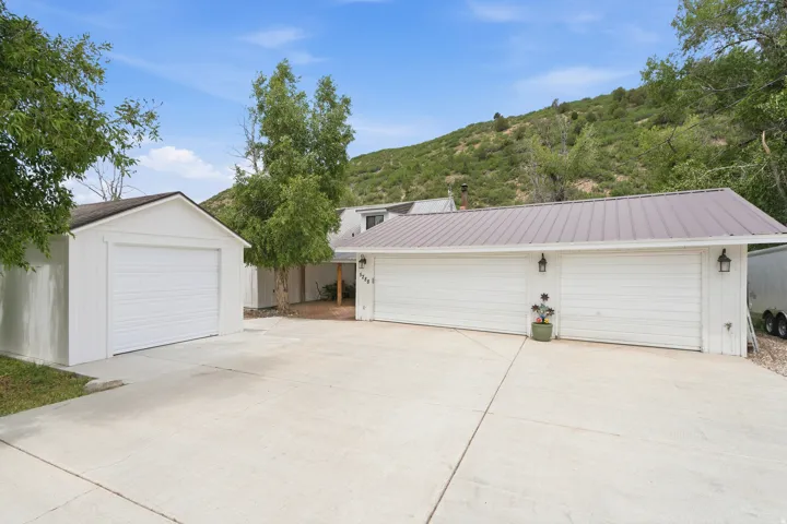 Expansive concrete driveway servicing a detached single-car garage and a two-car garage with a metal roof and exterior wall lanterns