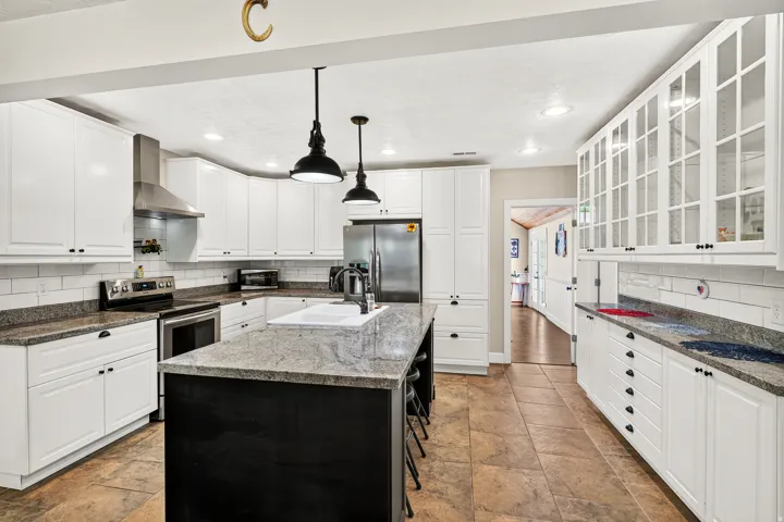 Spacious kitchen featuring white cabinetry, granite countertops, a central island with seating, stainless steel appliances, and tile flooring