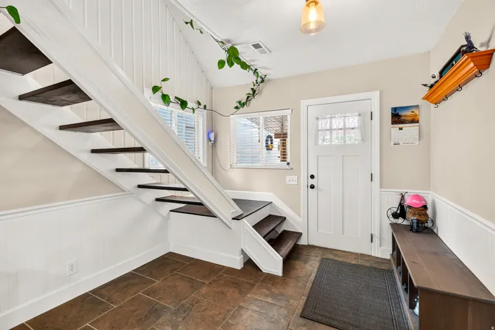 Entryway featuring brown tile flooring, white wainscoting, and a white paneled door with glass inserts