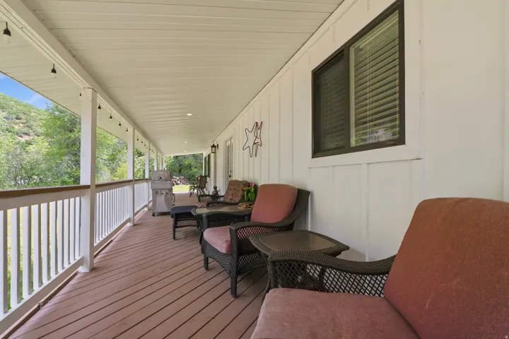 Expansive covered porch featuring a wood-finish deck, white railing, and exterior lighting