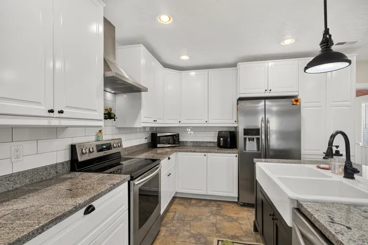 Modern kitchen featuring white shaker cabinetry, speckled countertops, stainless steel appliances, a subway tile backsplash, and a farmhouse sink