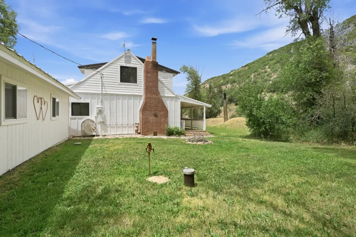 Expansive green lawn with a white board-and-batten home featuring a prominent brick chimney