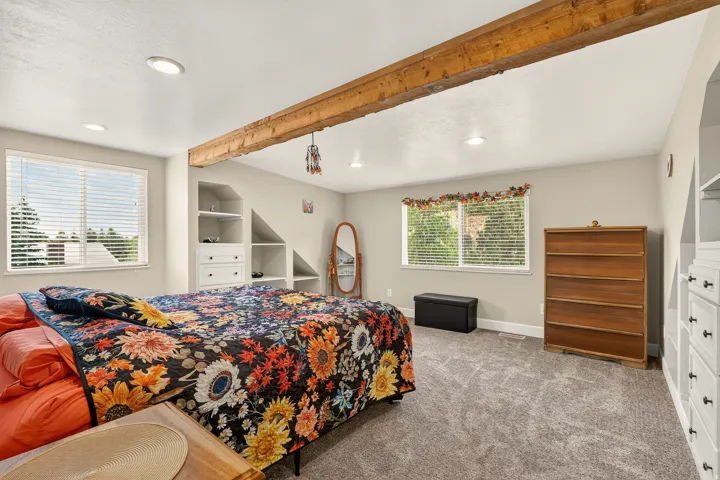 Spacious bedroom featuring a prominent wood ceiling beam and recessed lighting