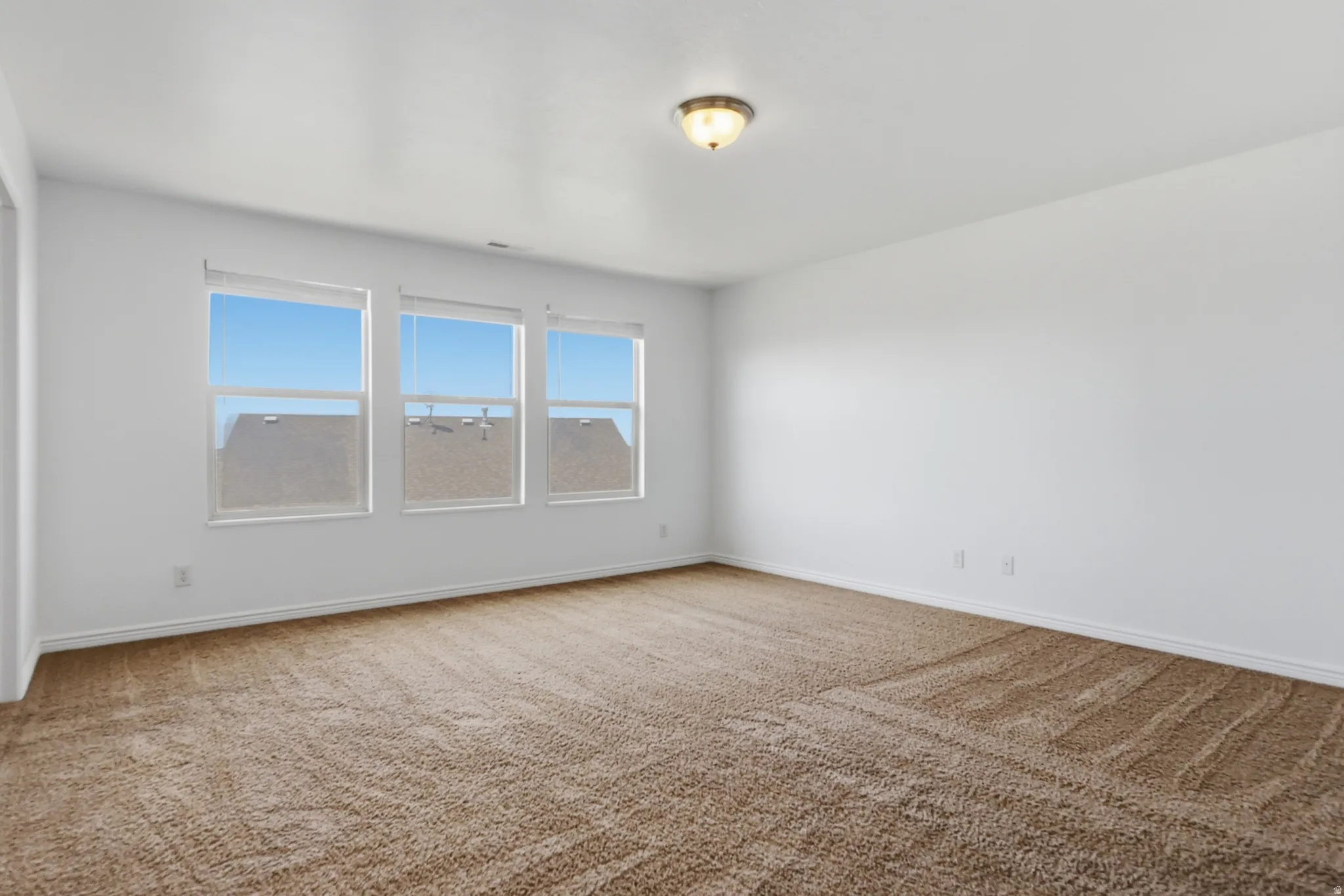 Spacious room featuring three large windows, neutral-toned carpeting, and a flush mount ceiling light fixture
