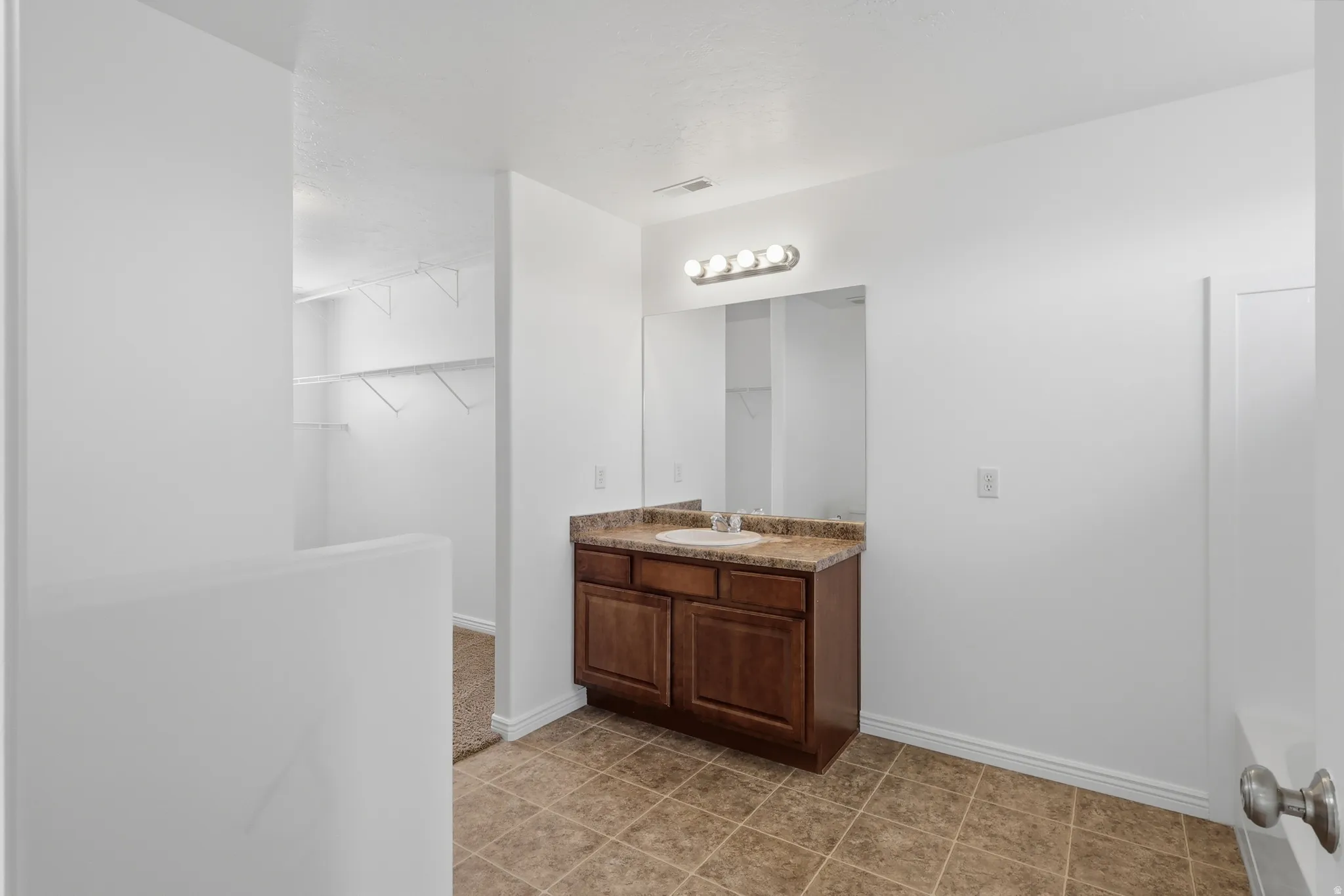 Bathroom vanity with a brown wood-finish cabinet and a light-colored countertop, featuring a rectangular mirror and a four-bulb light fixture