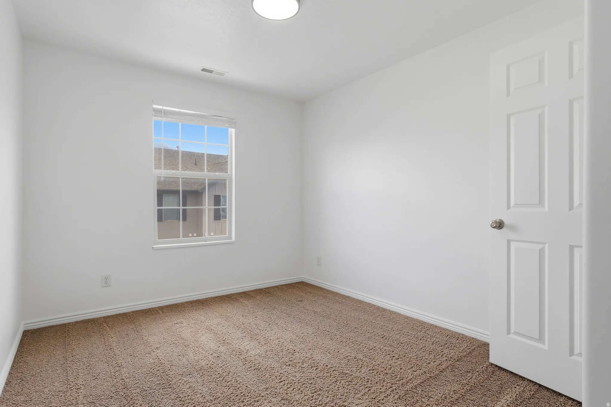 Bright interior space featuring a window with integrated blinds, plush carpet flooring, white painted walls, and a ceiling-mounted light fixture