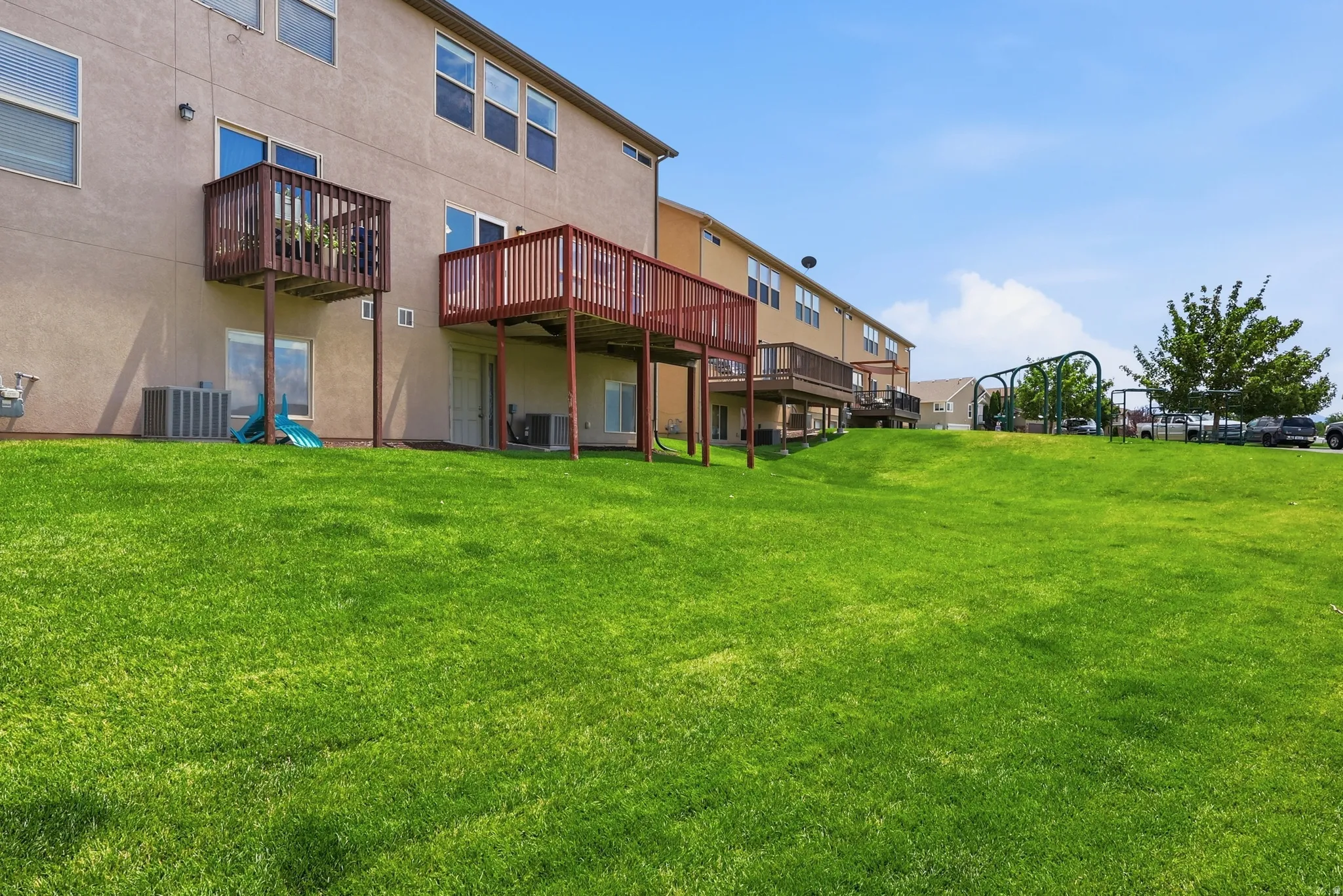 Expansive green lawn with a gradual incline, bordered by multi-story residential structures featuring individual elevated decks