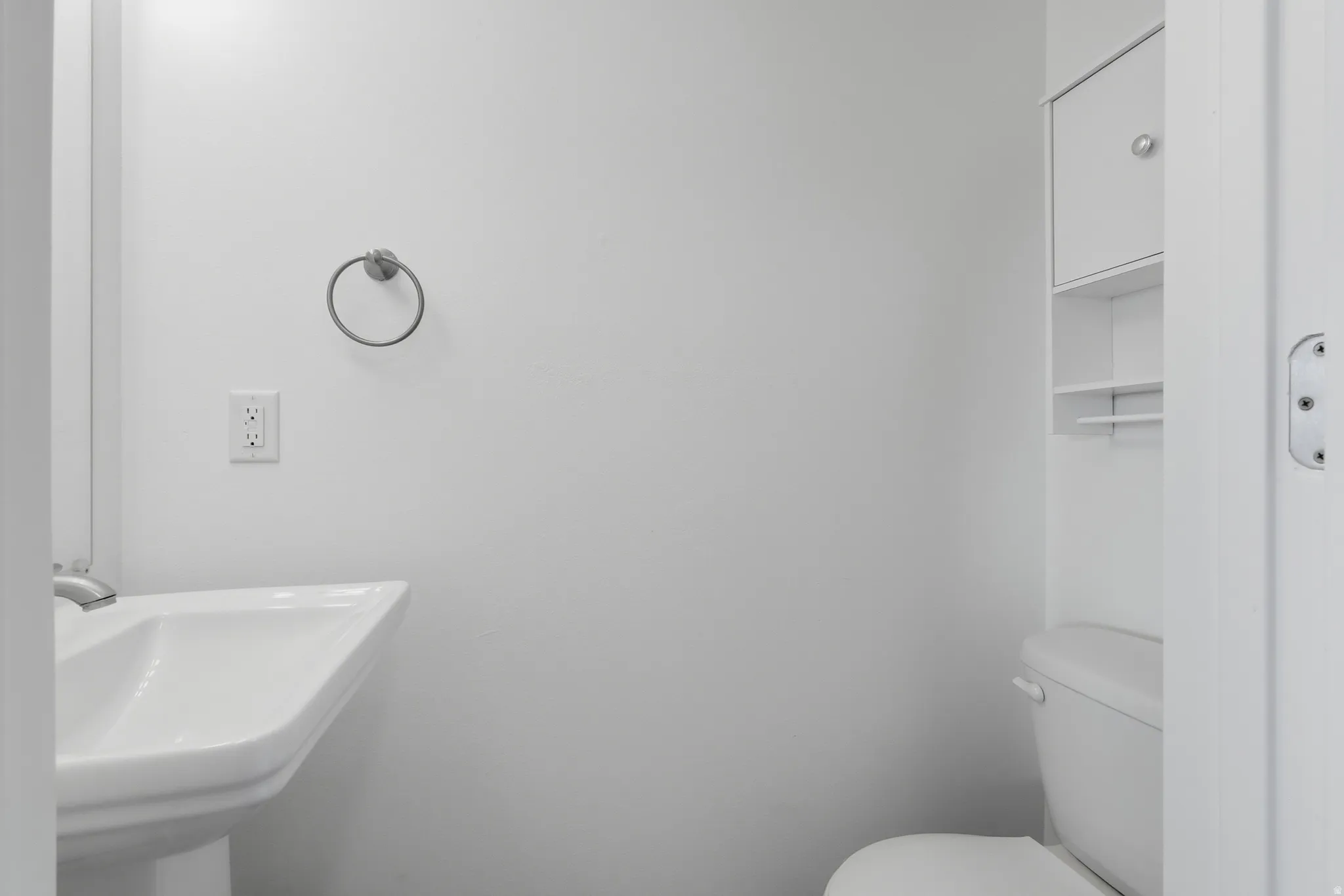 Bathroom featuring a white pedestal sink, white toilet, and integrated white shelving unit with a cabinet