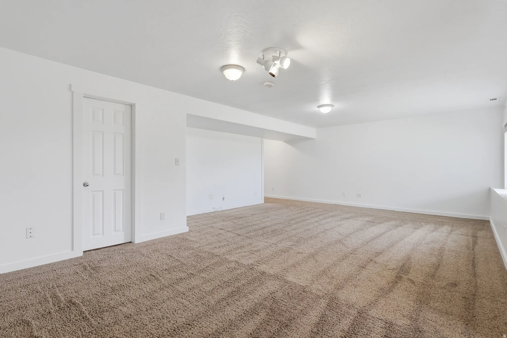 Spacious room with plush brown carpeting, white walls, and a six-panel interior door