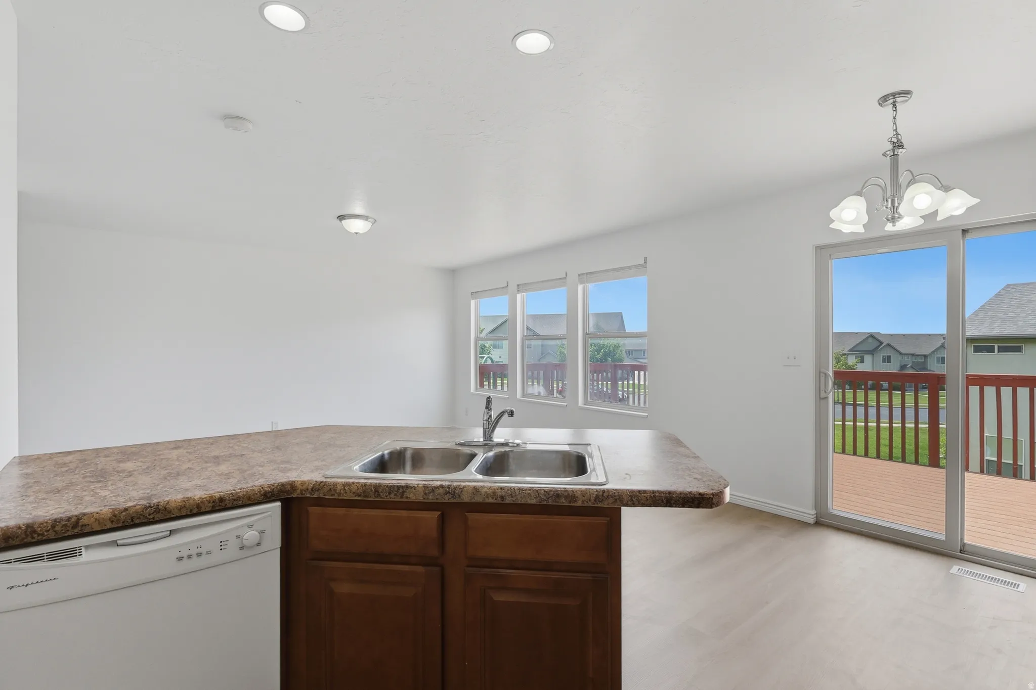 Kitchen counter with double basin sink and integrated dishwasher, featuring wood-finish cabinetry, recessed lighting, and a composite countertop