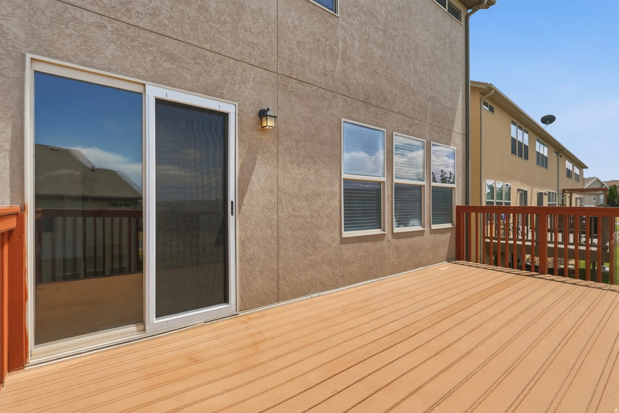Spacious outdoor deck featuring wood-finish flooring, a full sliding glass door with screen, and a wall-mounted exterior light fixture