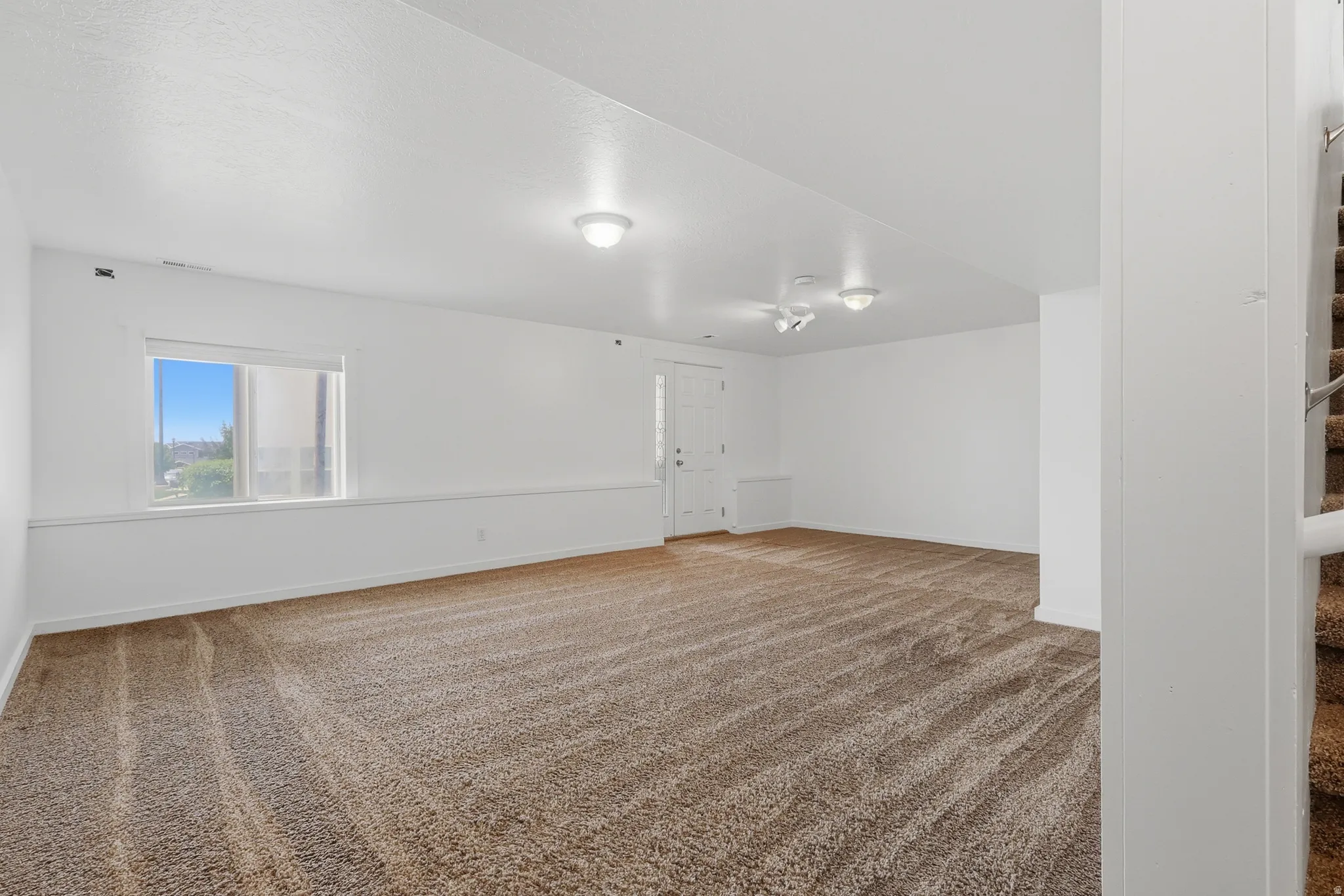 Spacious room with plush brown carpet, white walls, and a large window