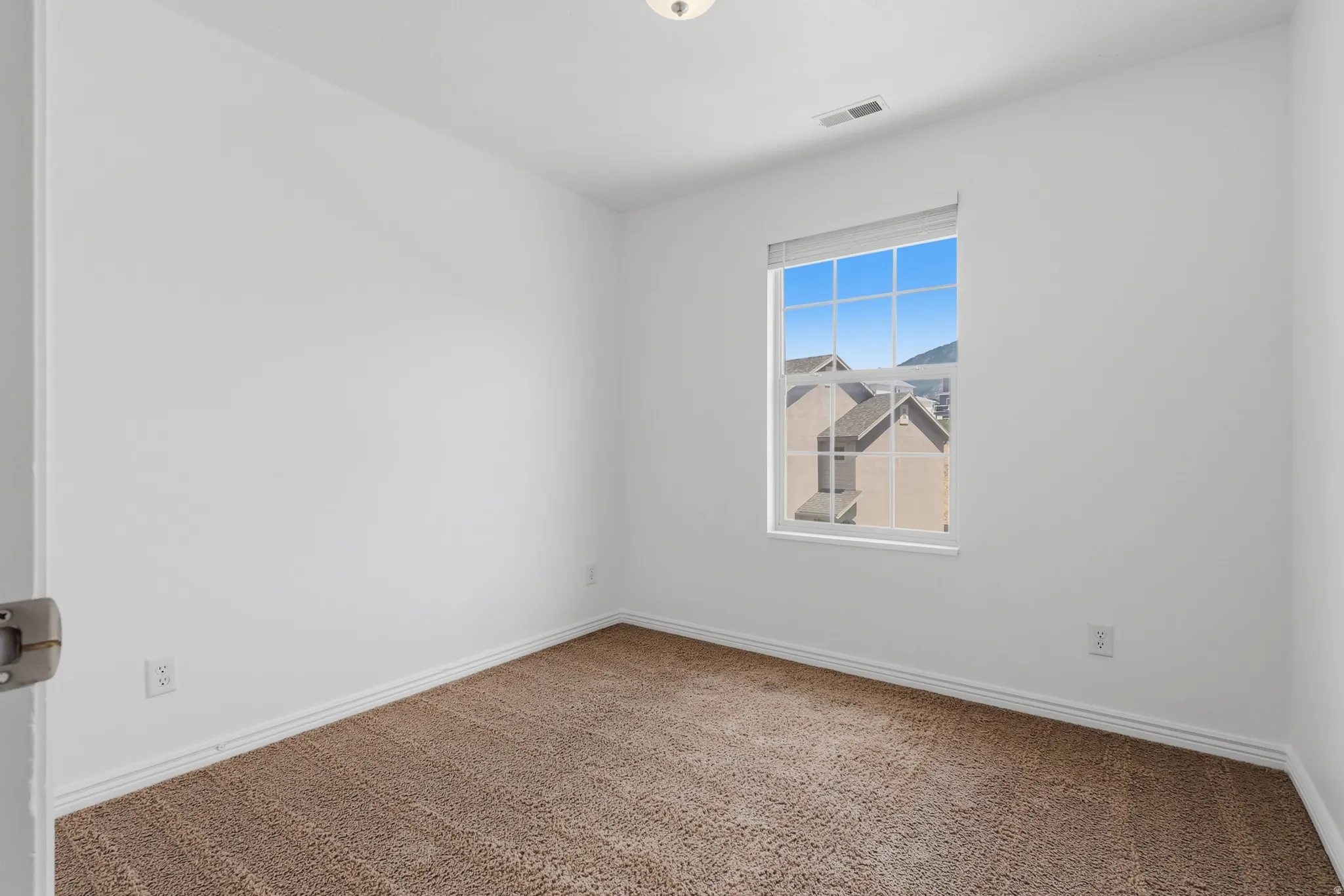Room featuring a window with grid panes, textured carpeting, white walls, and white baseboards
