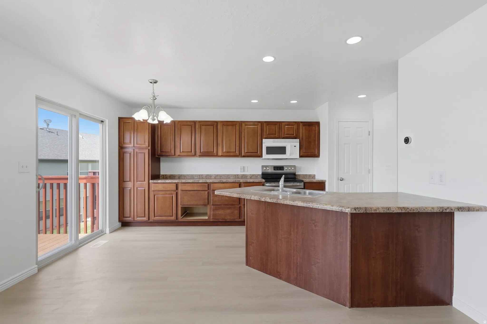 Kitchen featuring a central island with a multi-toned countertop, wood-finish flooring, recessed lighting, and a sliding glass door leading to an exterior deck