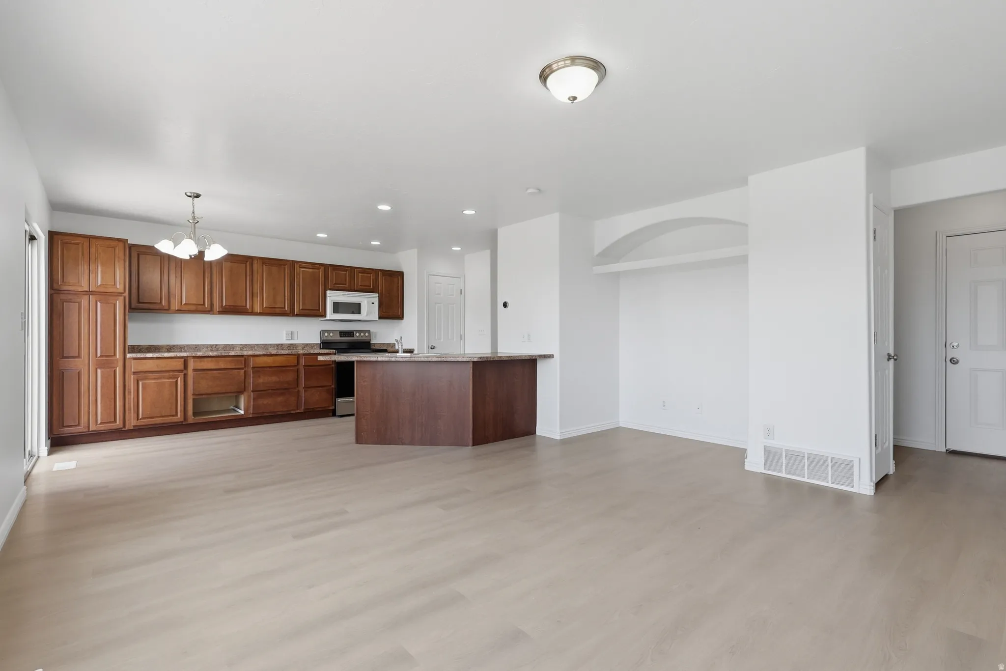 Open-concept living area featuring light wood-finish flooring, a kitchen with rich wood cabinetry, a central island, and a built-in microwave