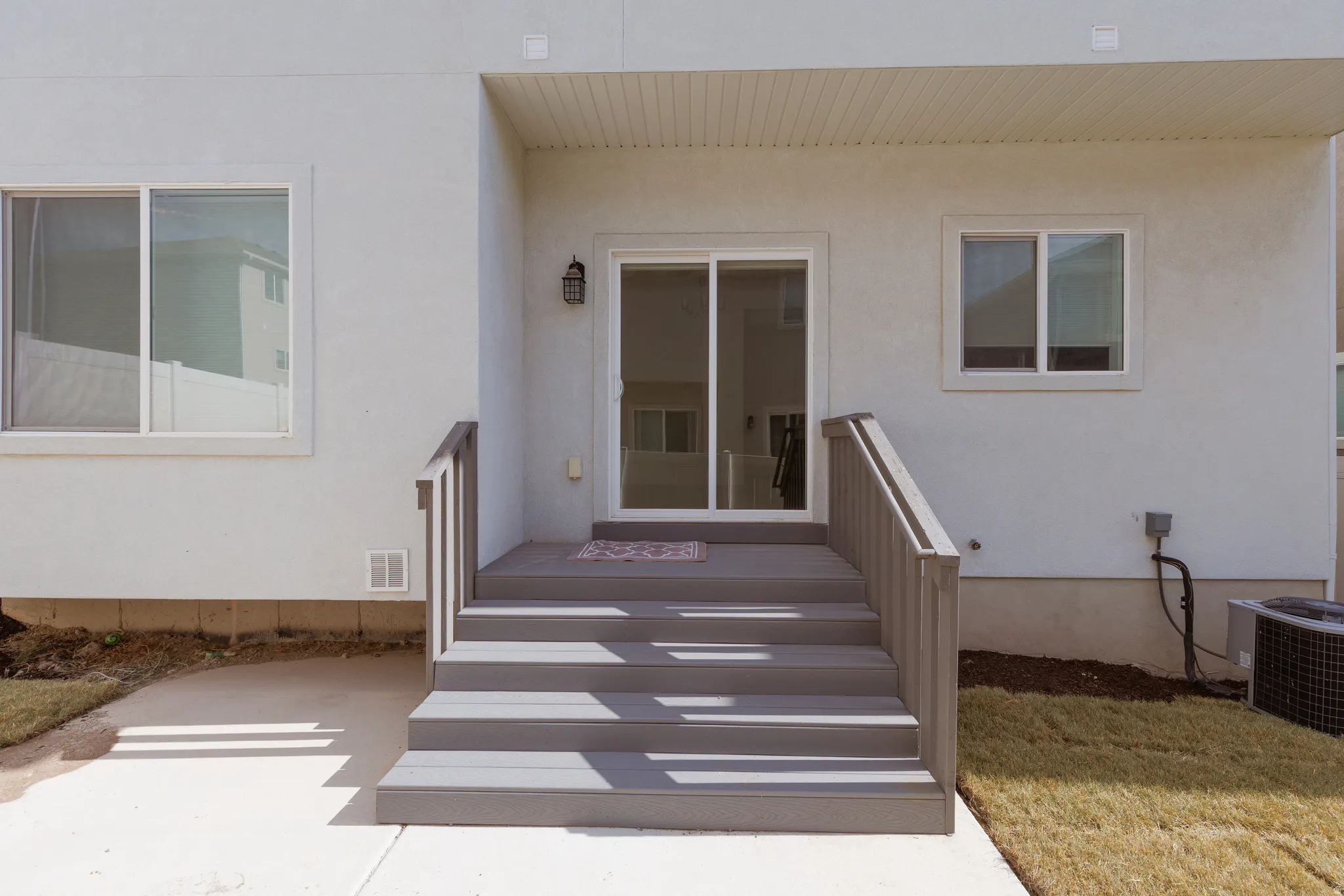 Rear exterior featuring light-colored stucco, a sliding glass patio door, and a multi-step composite deck with railings