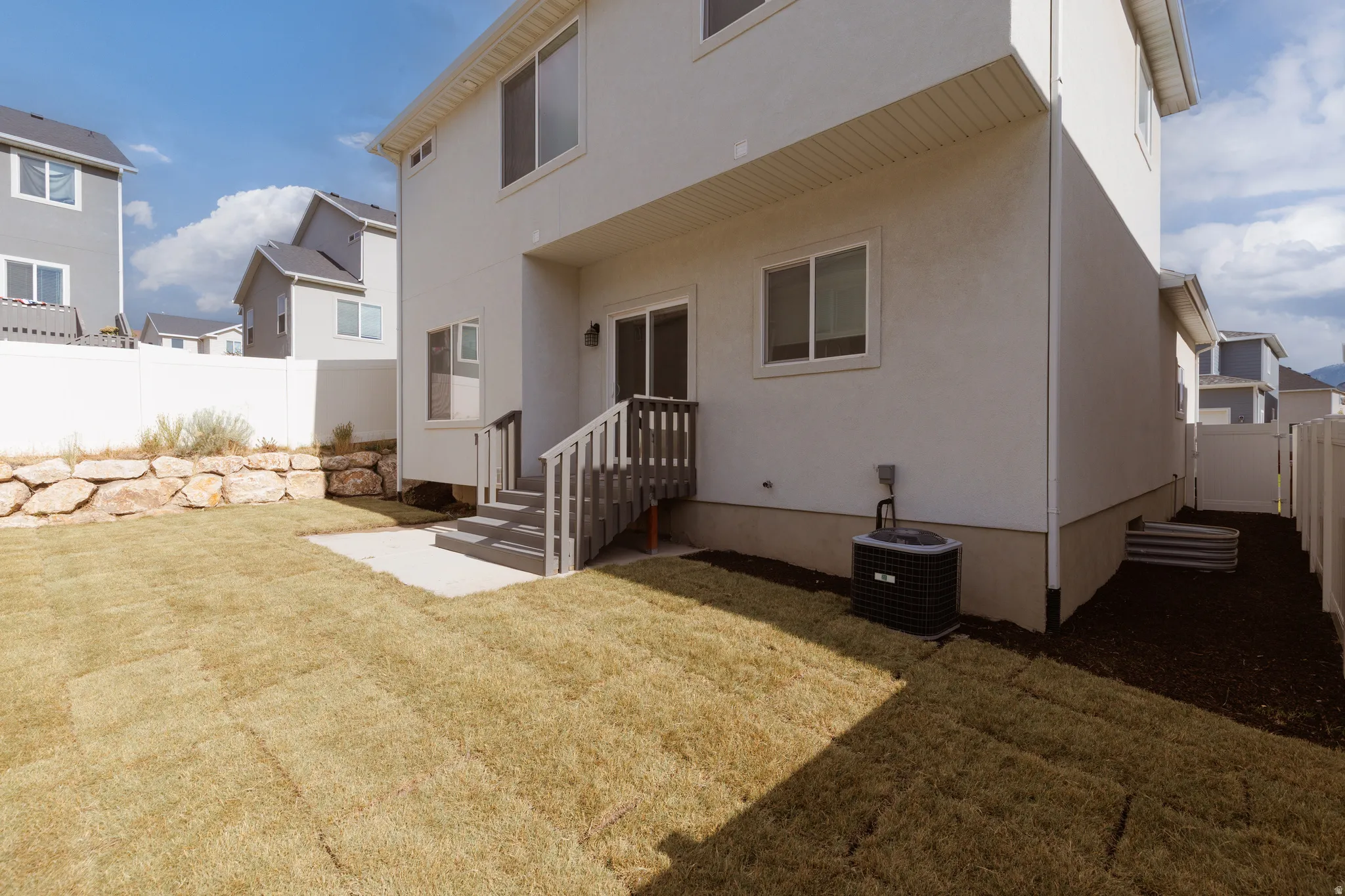 Rear exterior featuring a sliding glass door, private fenced yard, concrete patio, and rock retaining wall