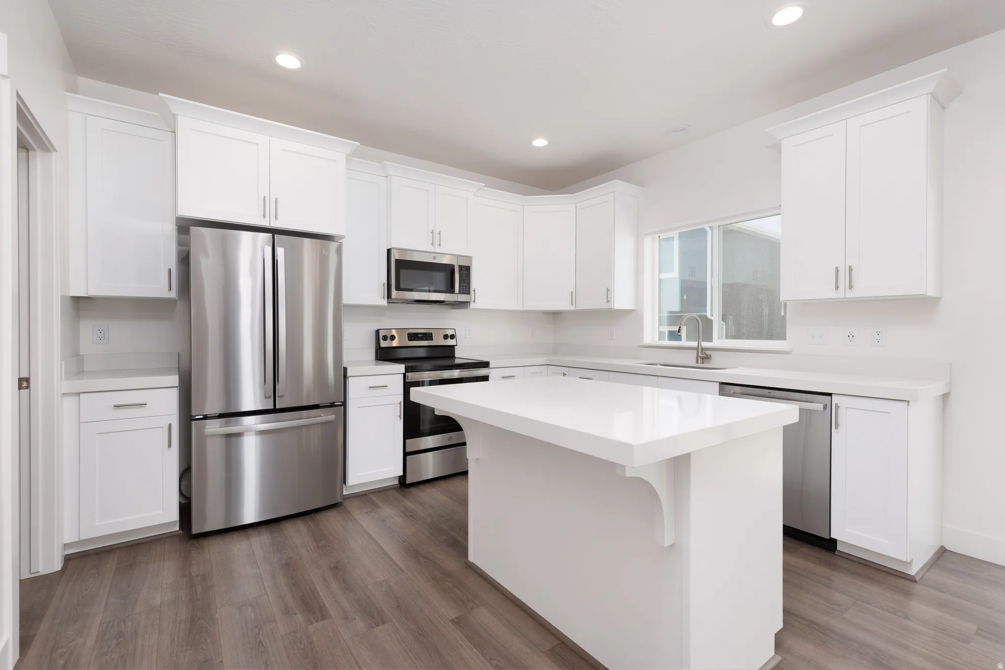 Kitchen featuring white cabinetry, stainless steel appliances, a center island, light countertops, and wood-finish flooring