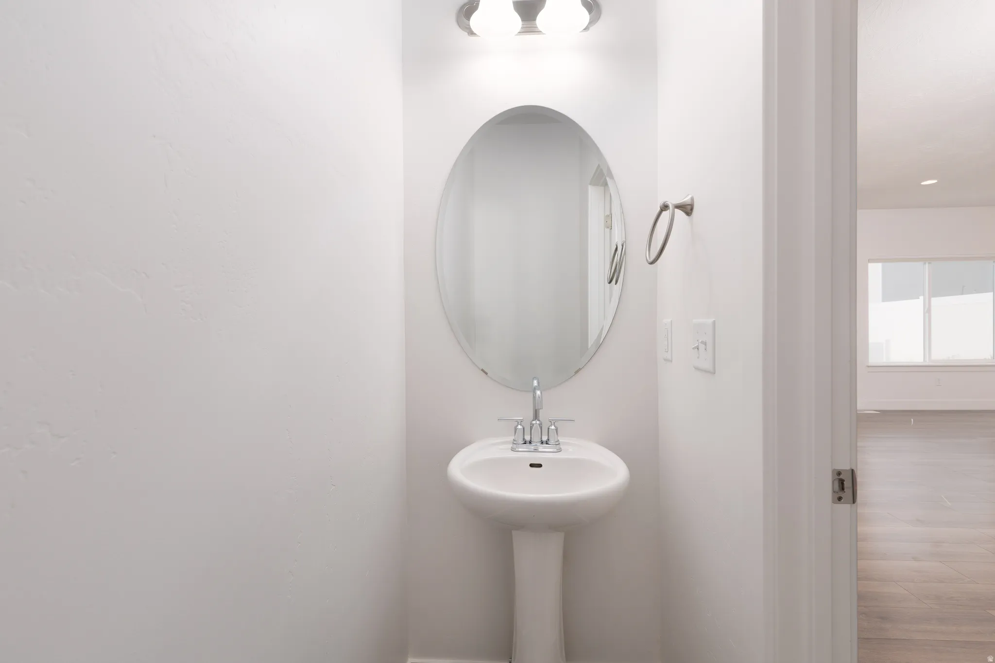Pedestal sink with chrome fixtures and an oval mirror, complemented by a contemporary wall-mounted light fixture and a brushed nickel towel ring