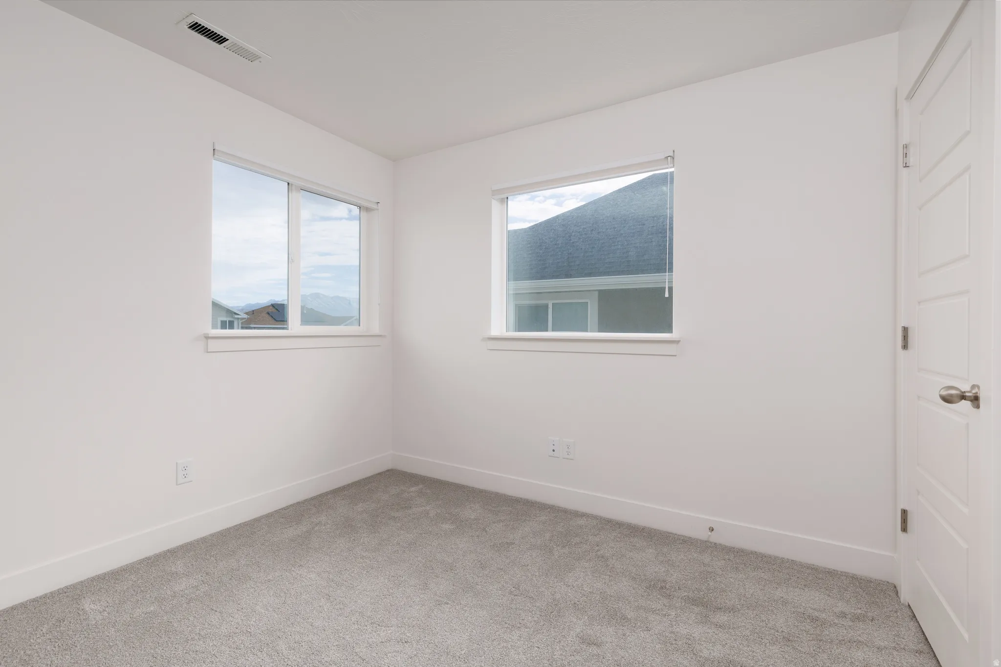 Bright interior space featuring two windows, light-toned carpet, white walls, and a multi-panel interior door