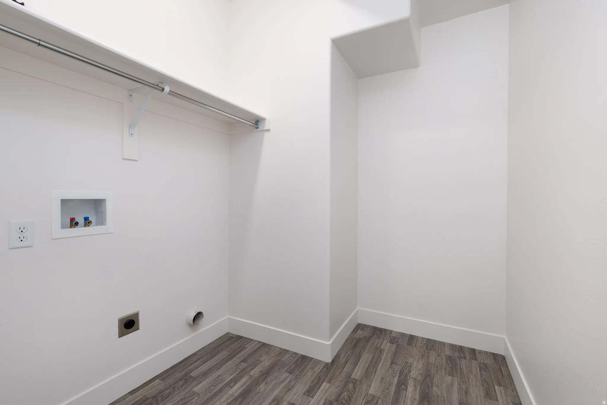 Dedicated utility area featuring wood-finish flooring, white walls, and a built-in shelf with a hanging rod