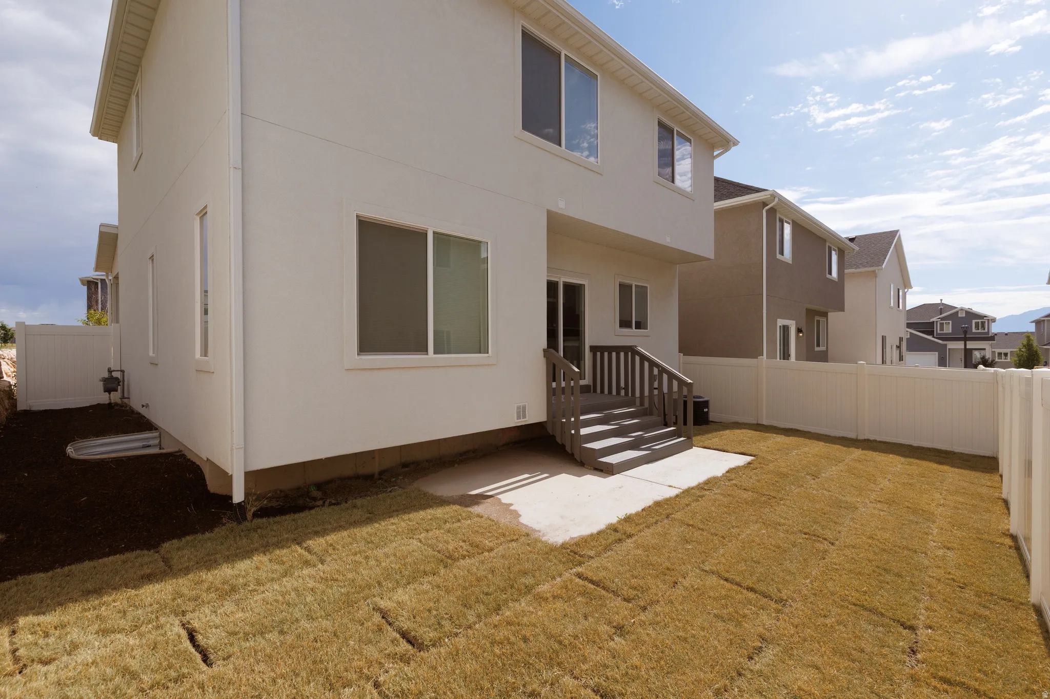 Rear exterior featuring a deck with steps, a concrete patio, and a newly installed lawn area