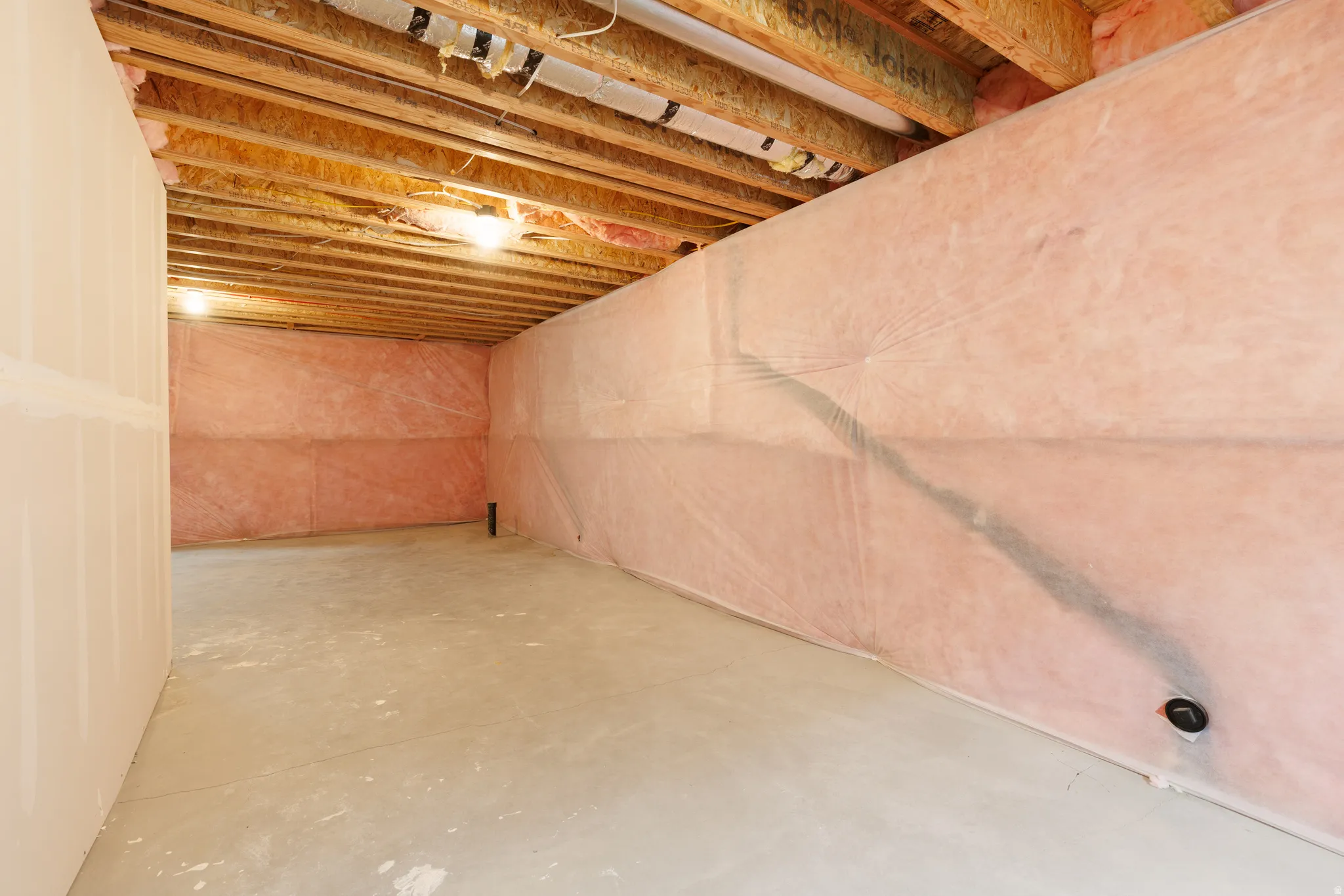 Unfinished basement featuring exposed wood joists, concrete flooring, and insulated walls