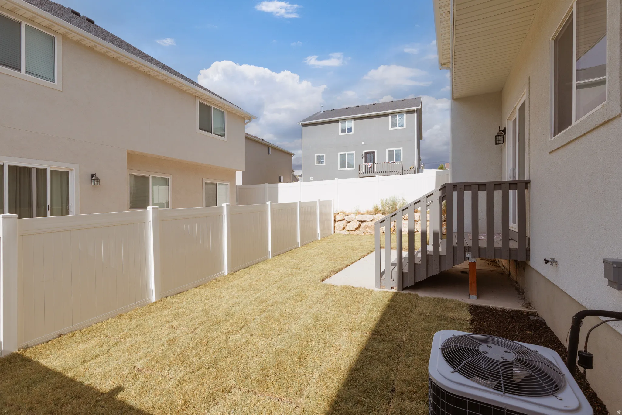 Expansive backyard featuring a manicured lawn, white vinyl fencing, and a wooden staircase leading to a lower patio