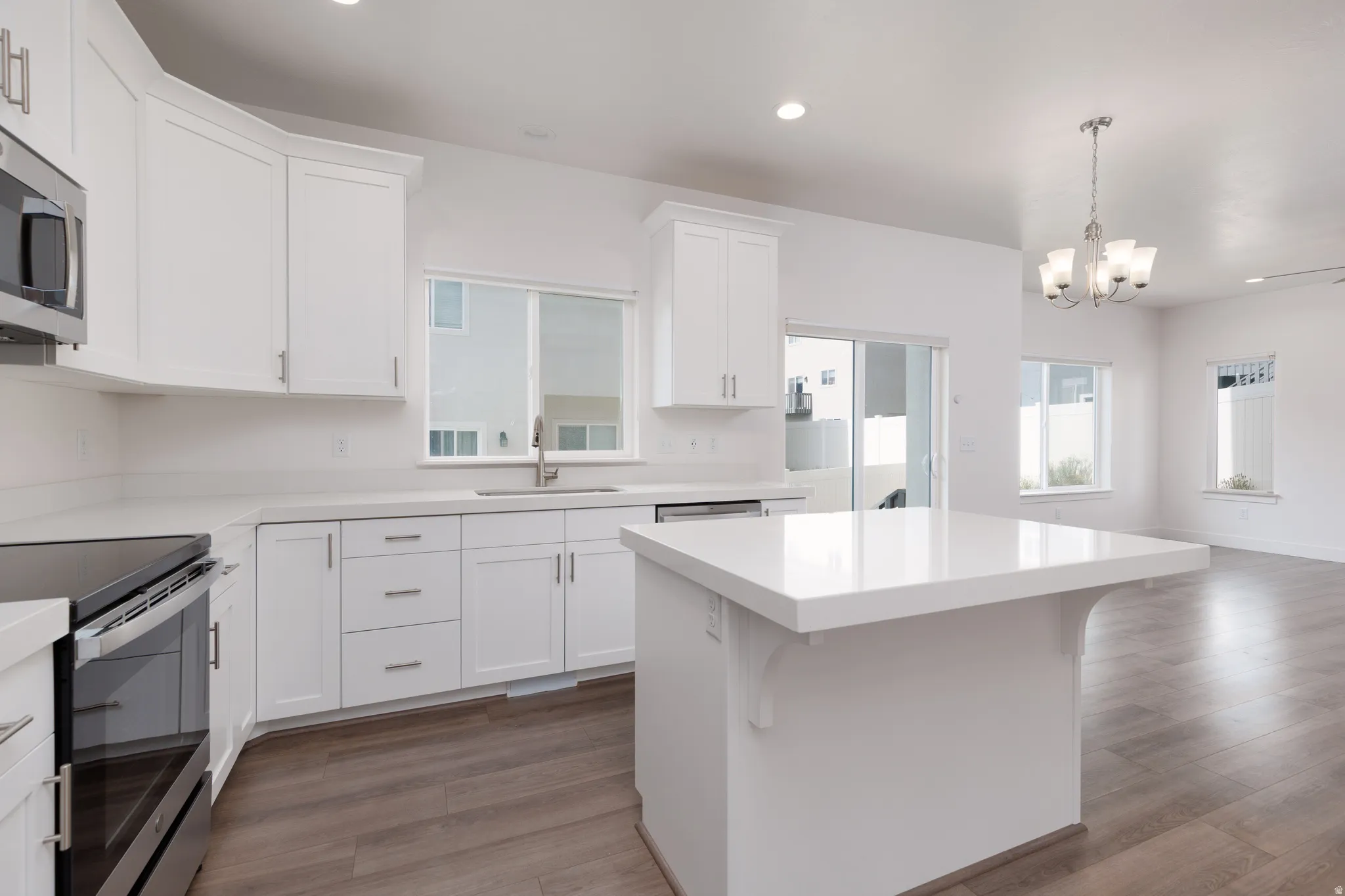 Bright kitchen featuring white shaker cabinetry, stainless steel appliances, a center island with a white countertop, and wood-finish flooring