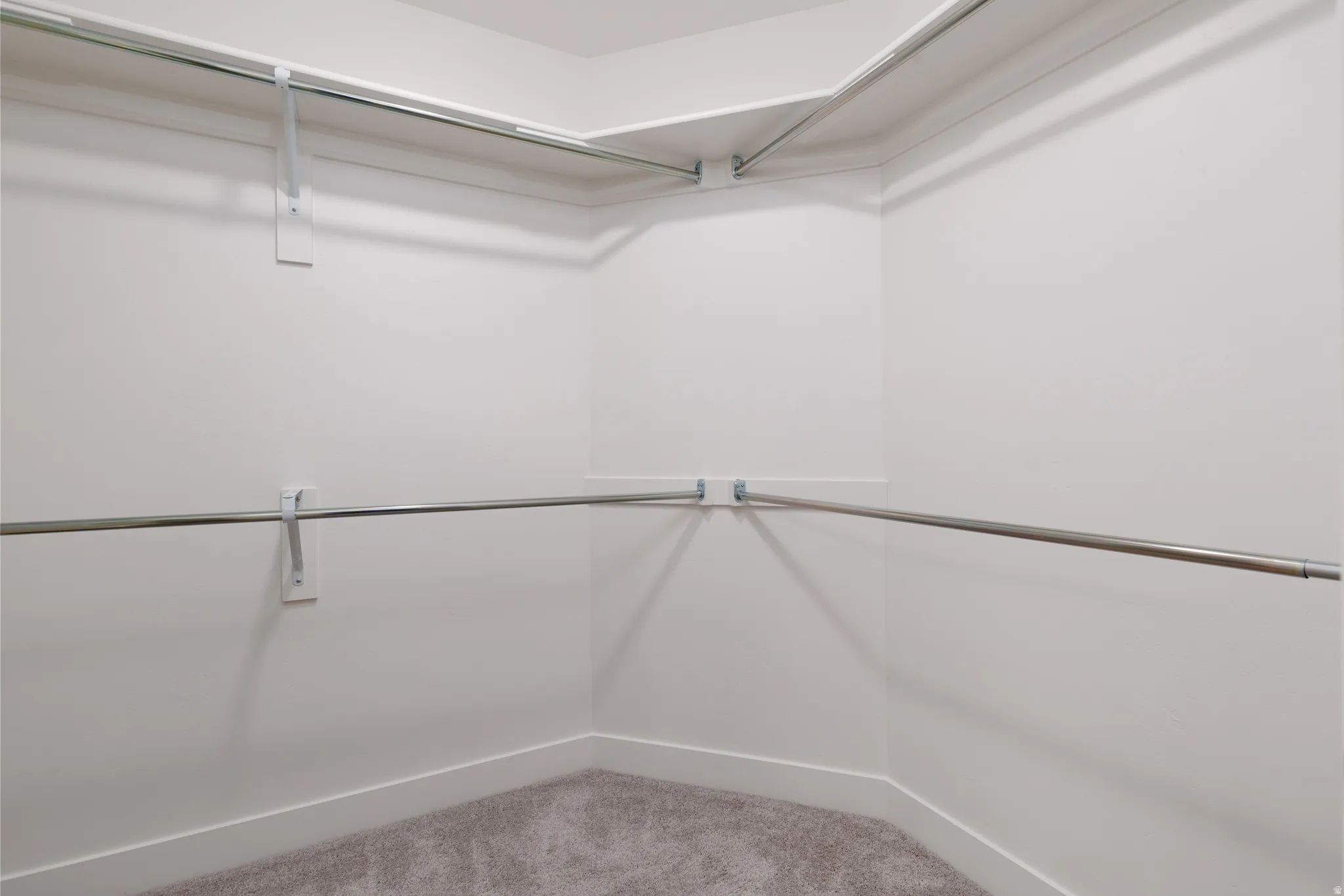 Walk-in closet with light gray carpet flooring, white painted walls, white baseboards, and two levels of metal hanging rods