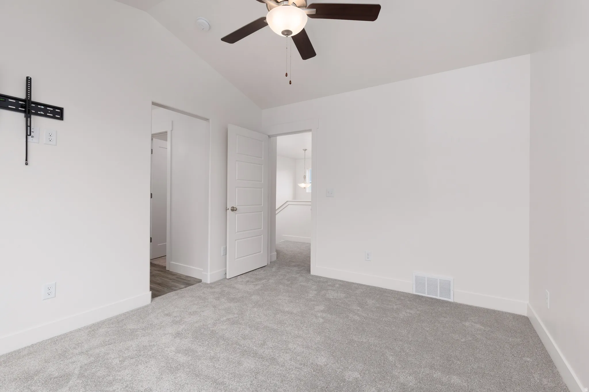 Spacious room featuring vaulted ceilings, light gray carpeting, a ceiling fan with integrated lighting, and crisp white trim