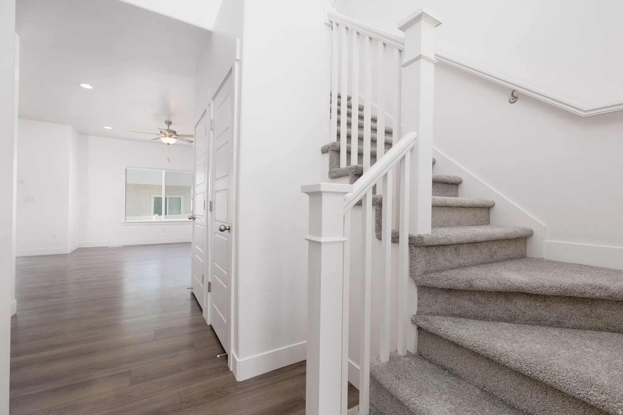 Carpeted staircase with white balusters and handrail, complementing the wood-finish flooring and recessed lighting