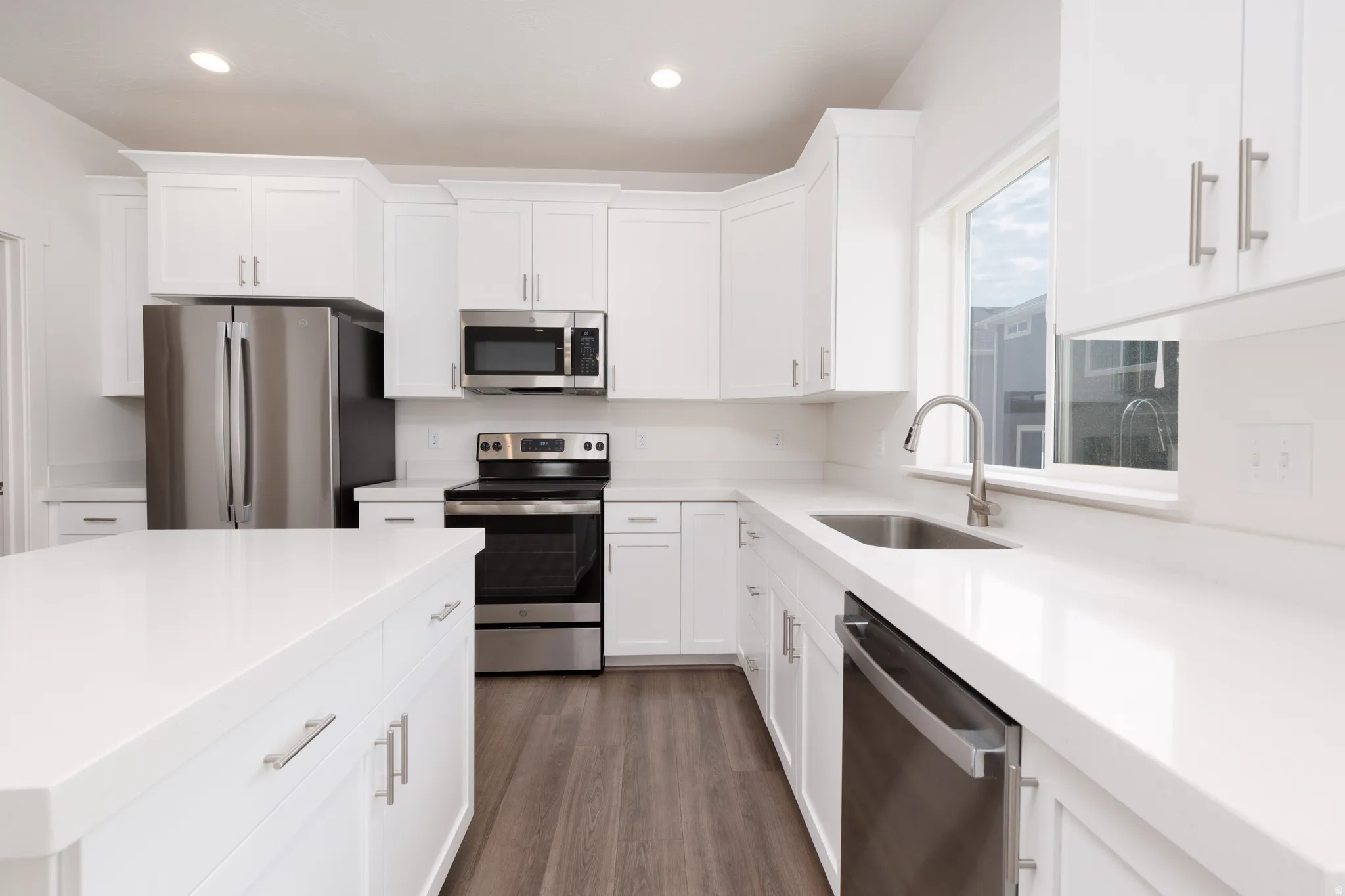 Modern kitchen featuring bright white cabinetry, stainless steel appliances, and wood-finish flooring