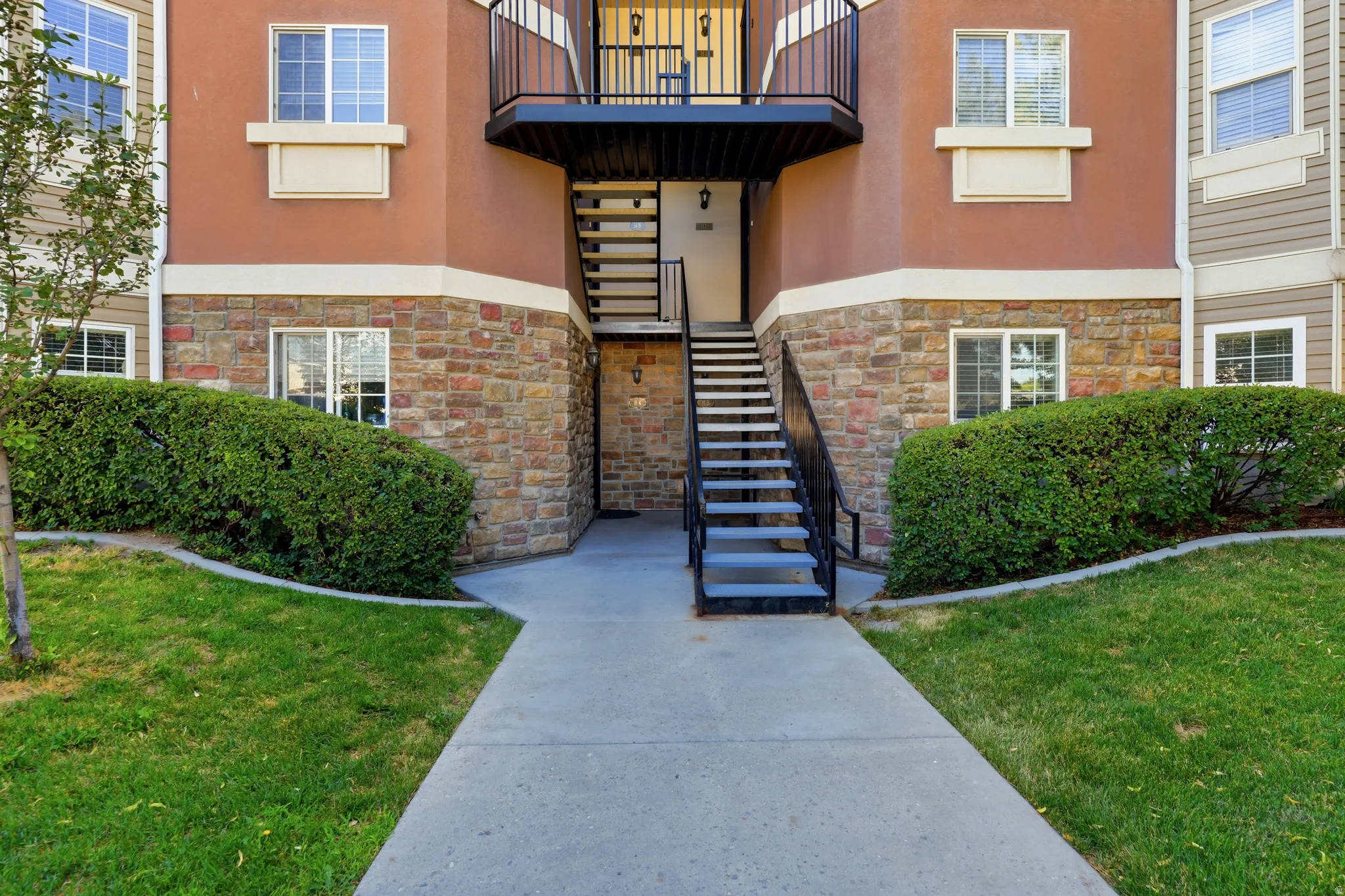 Building exterior featuring a concrete walkway, manicured shrubs, and a lawn
