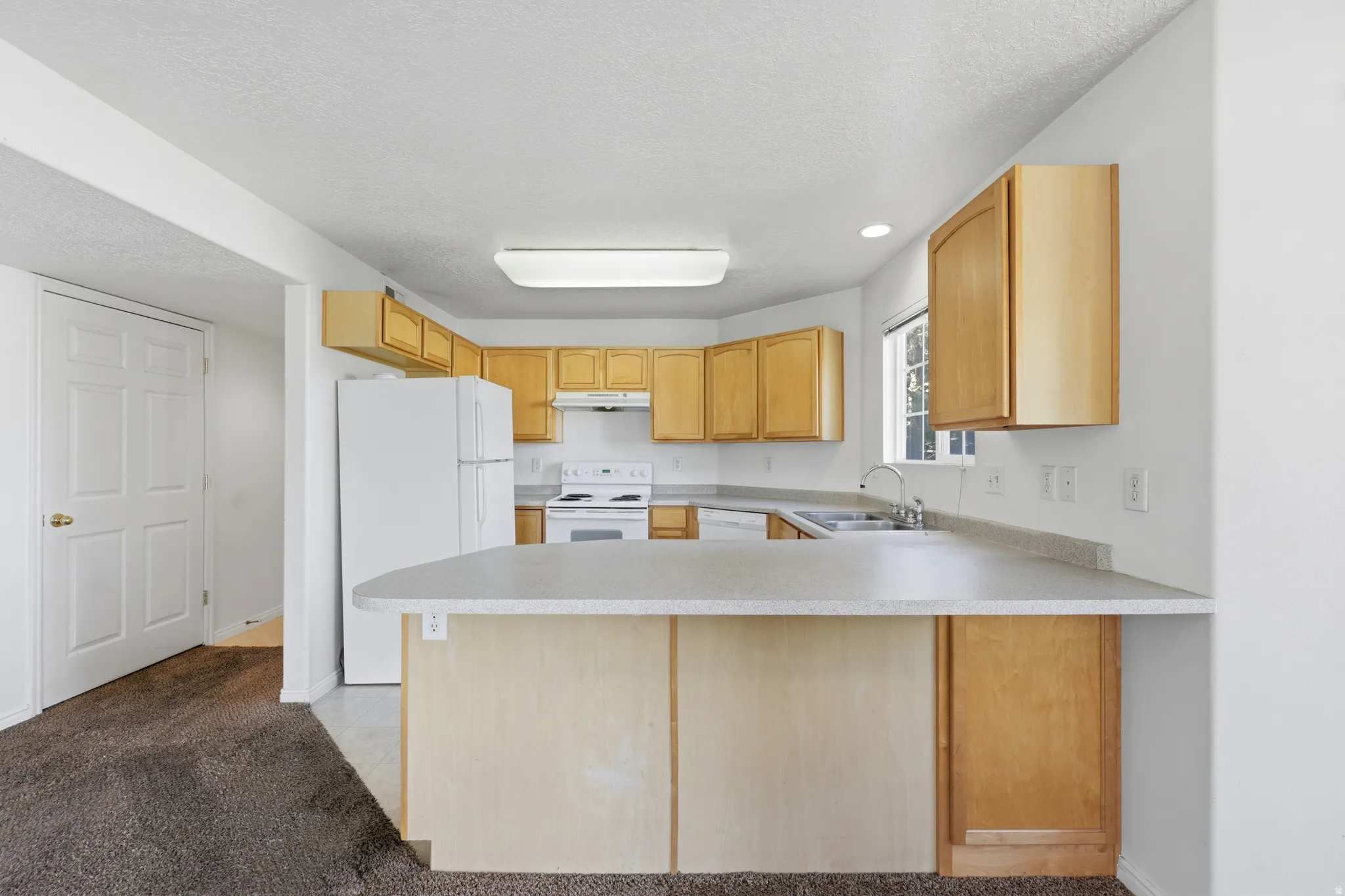 Kitchen featuring a breakfast bar with a light gray countertop, wood-finish cabinetry, a double basin sink, and a four-burner electric range