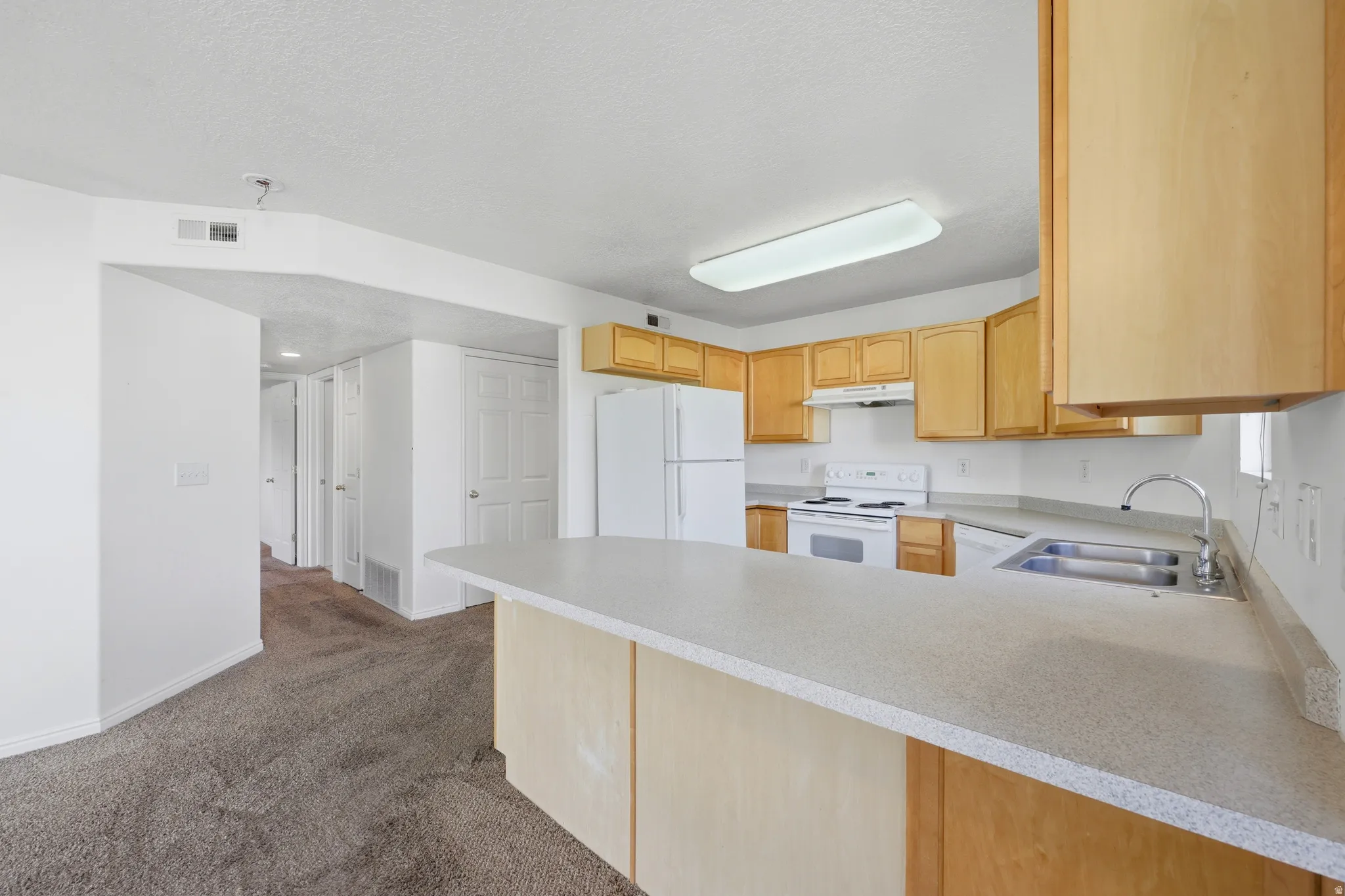 Kitchen featuring light wood cabinetry, white appliances, dual basin sink, and ample countertop space