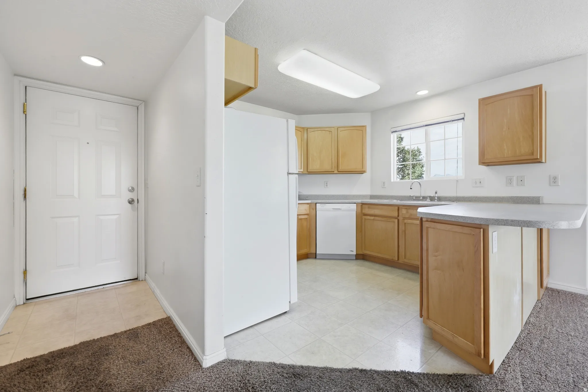 Kitchen featuring light wood-finish cabinetry, white appliances, and a light-toned countertop with an integrated breakfast bar