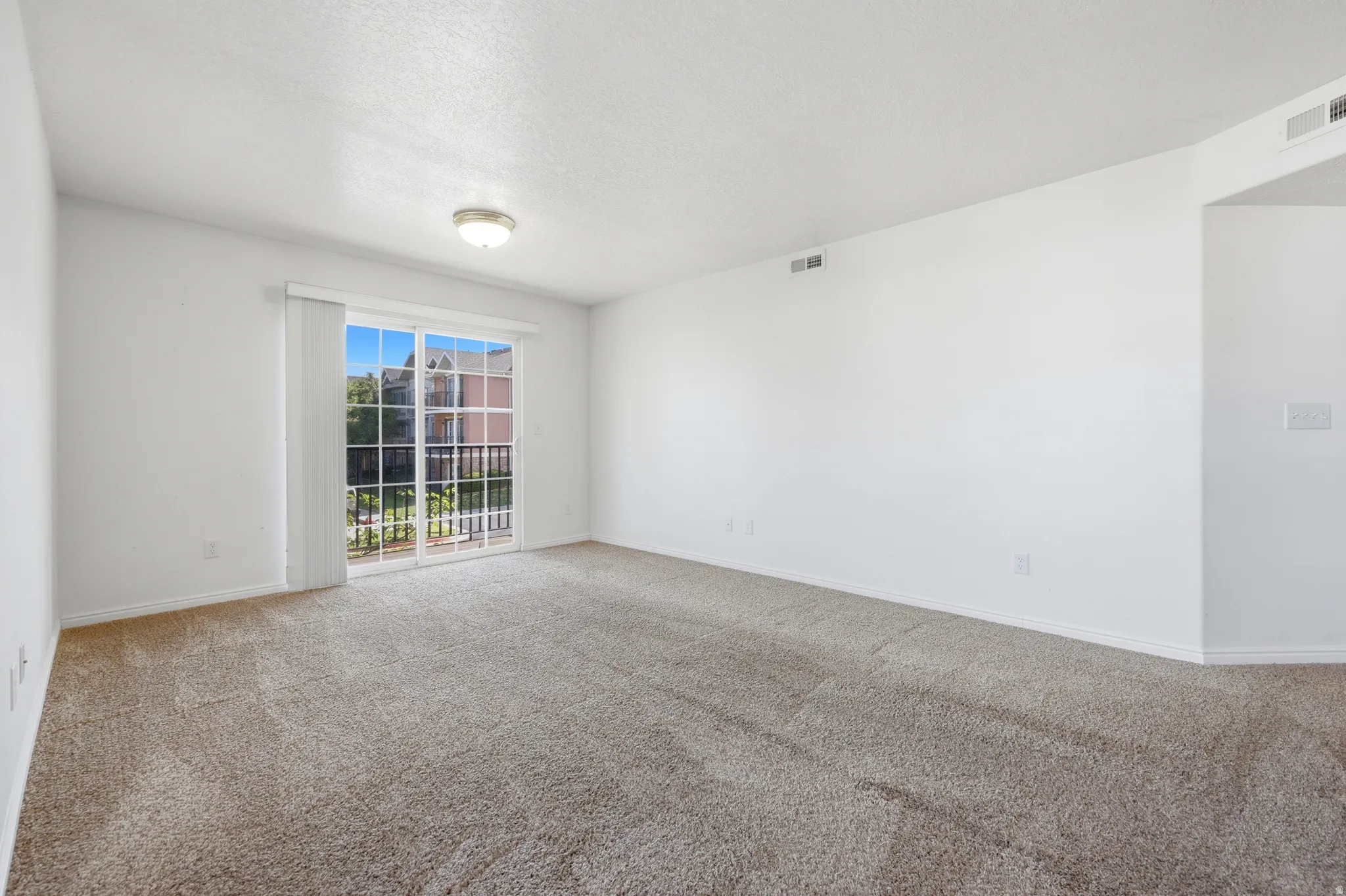 Spacious room featuring neutral carpet flooring, white walls, and a sliding glass door with balcony access