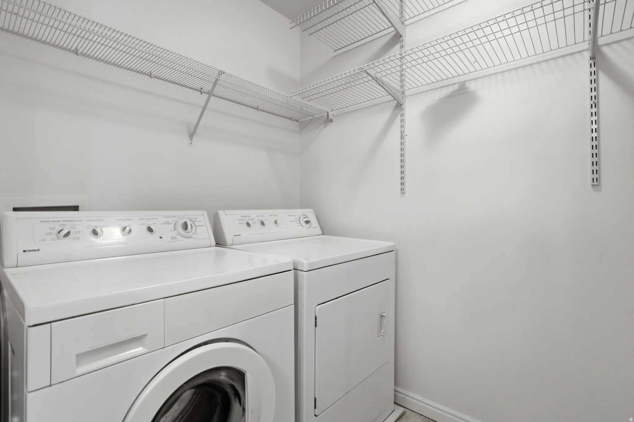 Dedicated laundry area featuring a front-loading washing machine, a dryer, and wire shelving for organized storage