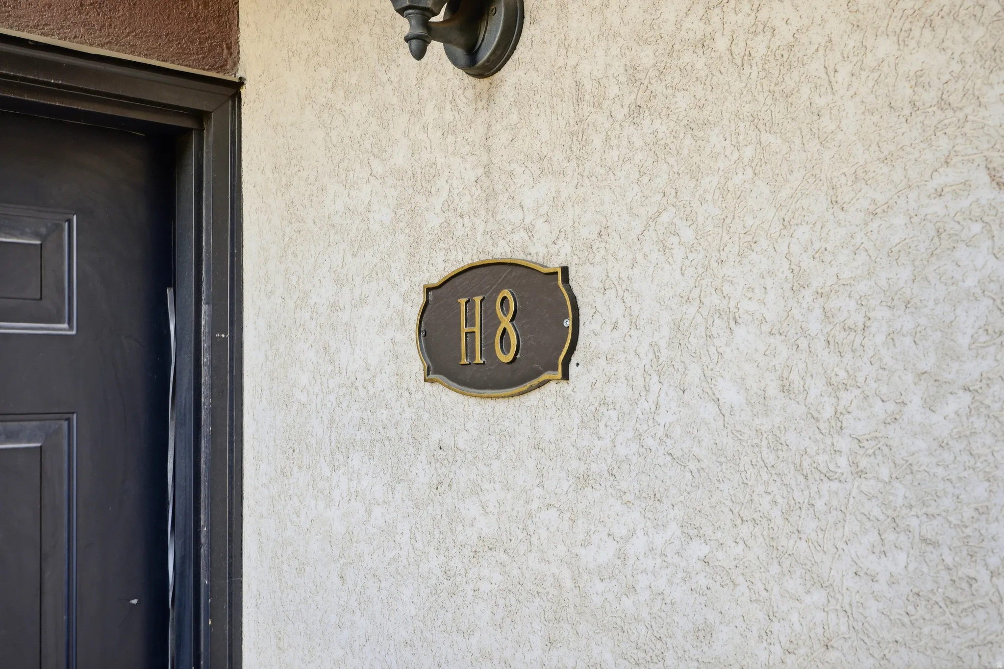 Exterior stucco wall featuring a decorative wall sconce and a metal address plaque