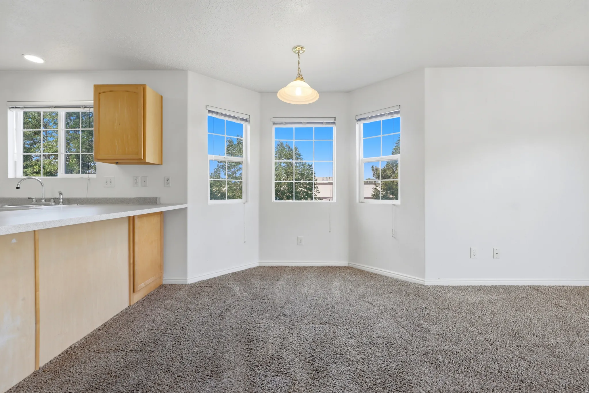 Dining area featuring a bay window with three large windows, a central hanging pendant light fixture, and plush carpeting