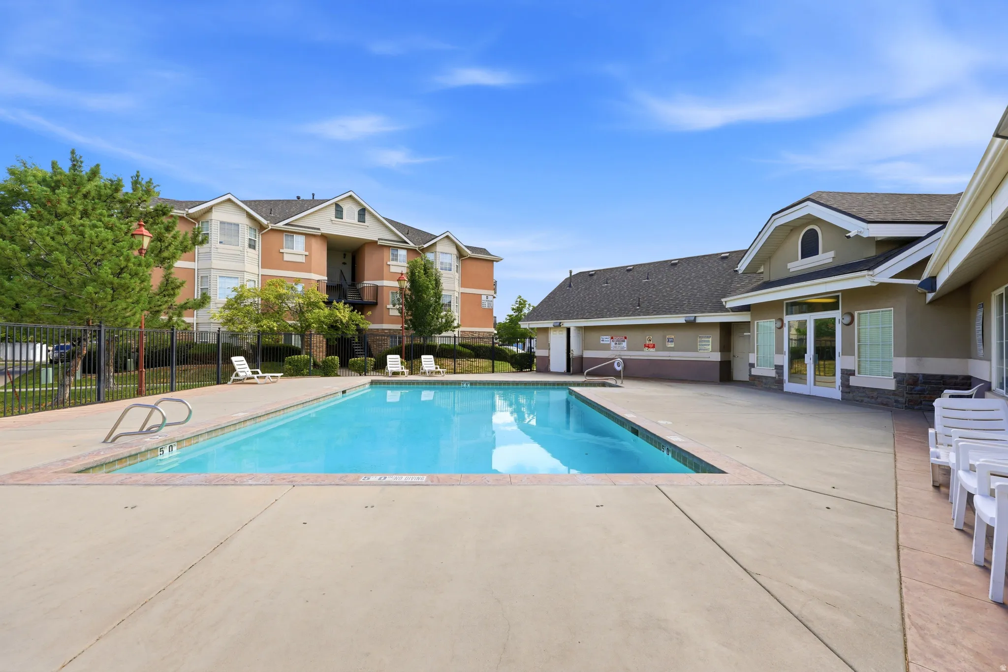 Outdoor swimming pool with concrete decking, surrounded by multiple lounge chairs and a perimeter fence