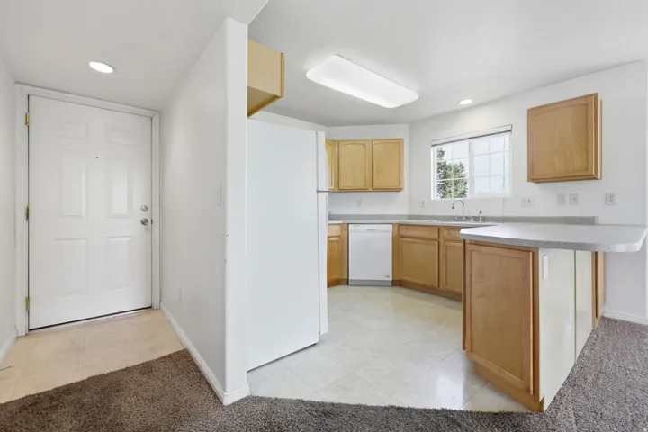 Kitchen featuring light wood-finish cabinetry, white appliances, and a light-toned countertop with an integrated breakfast bar