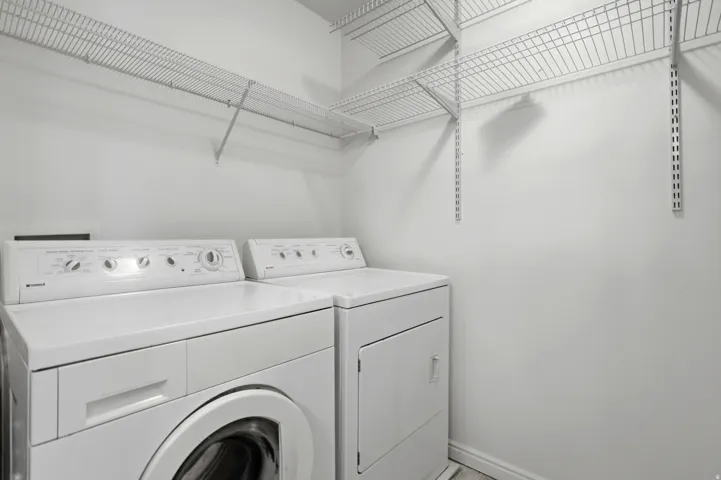 Dedicated laundry area featuring a front-loading washing machine, a dryer, and wire shelving for organized storage